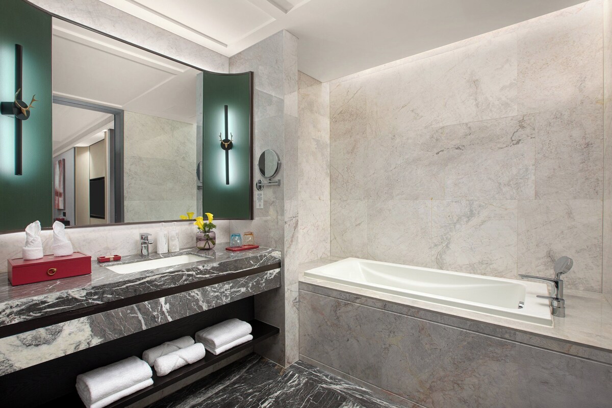 A modern bathroom with a marble sink, a large mirror, a bathtub, and neatly folded towels.