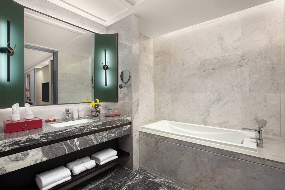 Ein modernes Badezimmer mit Marmorwaschbecken, einem großen Spiegel, einer Badewanne und ordentlich gefalteten Handtüchern.