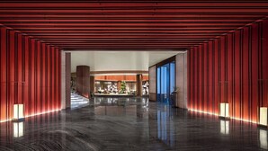 A modern lobby with a reflective floor, red paneling, and a central seating area with a staircase.
