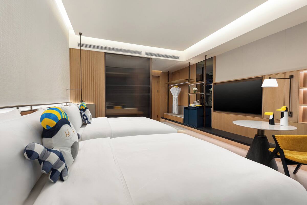 Habitación de hotel con dos camas, una mesita, una silla, un televisor y un armario.