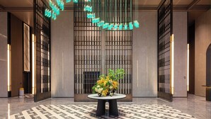 Un hall d’entrée au design moderne, avec une table centrale agrémentée d’un arrangement floral, un sol à motifs géométriques et un luminaire contemporain.