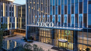 Un hôtel moderne, reconnaissable à son grand panneau « VOCO », à ses larges baies vitrées et à son hall d’entrée bien éclairé.