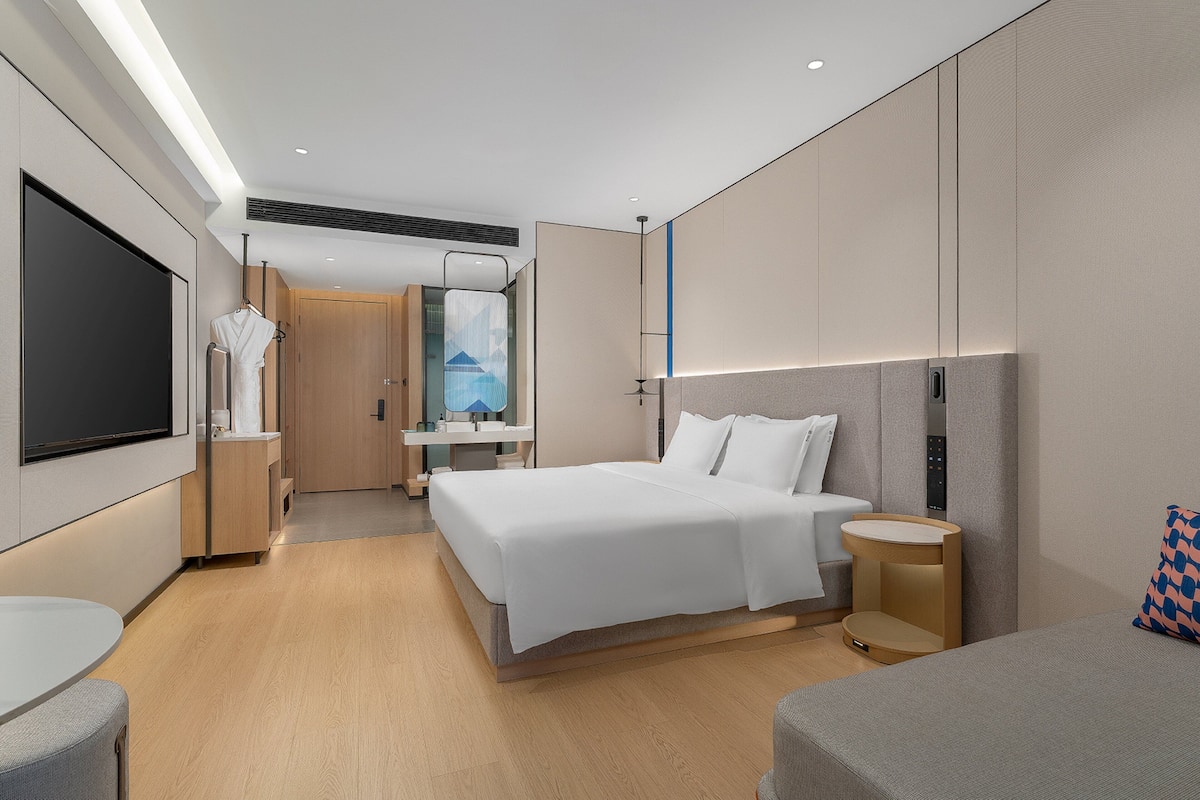 Ett modernt hotellrum med en stor säng, sängbord, en TV och ett badrum med dusch och toalett.