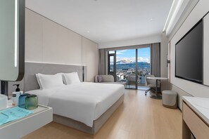 A modern hotel room with a large bed, a desk, a TV, and a balcony with a mountain view. - Holiday Inn Express Lijiang Ancient Town by IHG (Lijiang)
