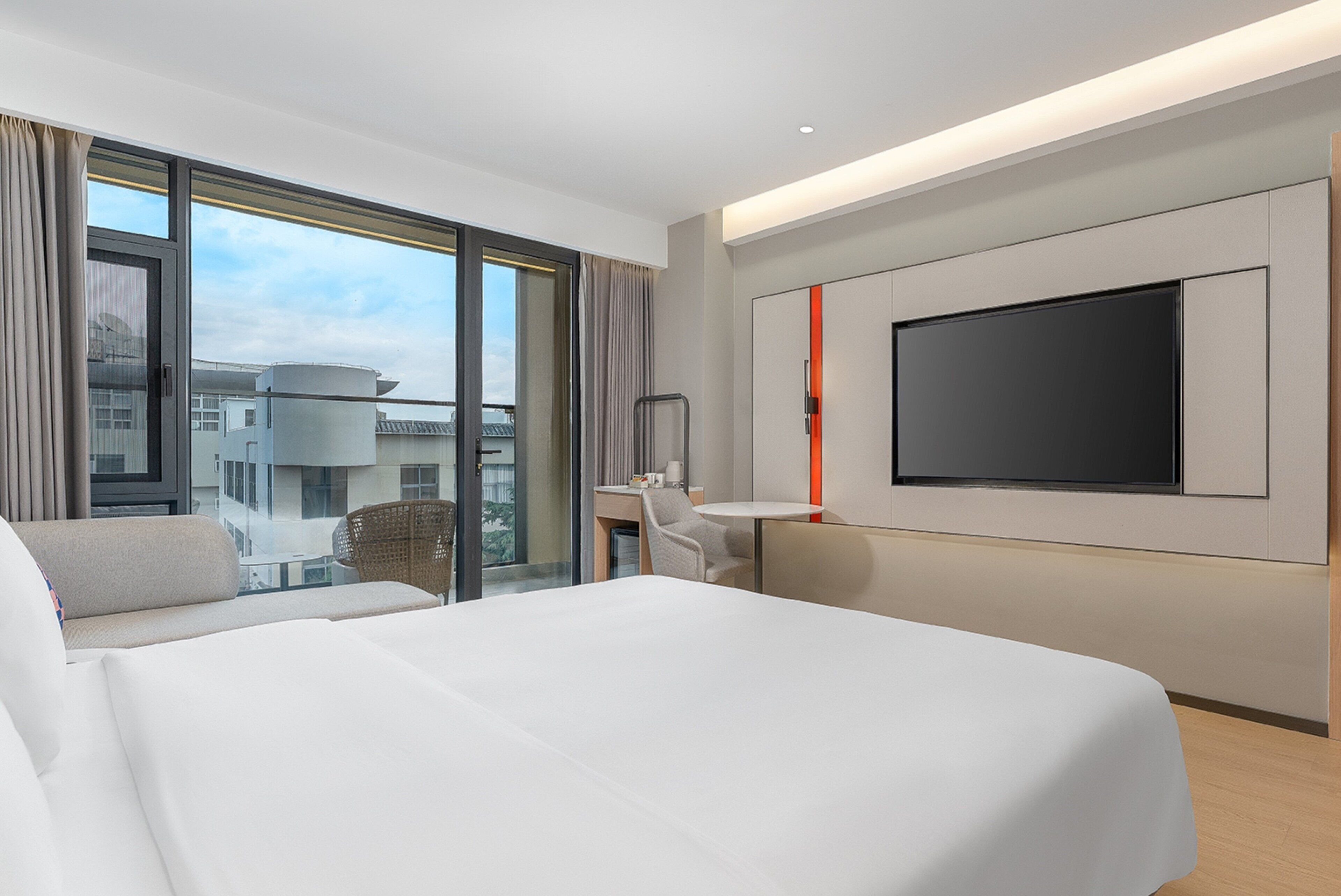Una habitación de hotel moderna con una cama grande, un escritorio, una silla y un televisor montado en la pared.