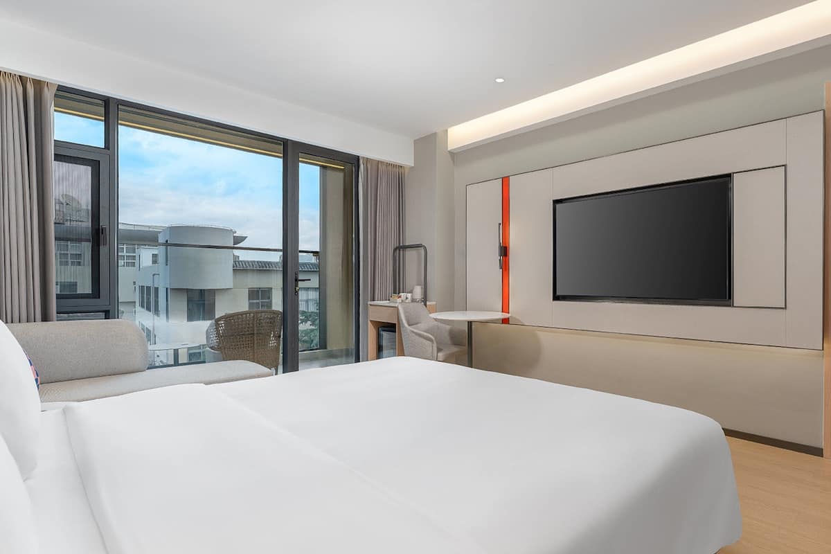 Ett modernt hotellrum med en stor säng, ett skrivbord, en stol och en tv som är monterad på väggen.