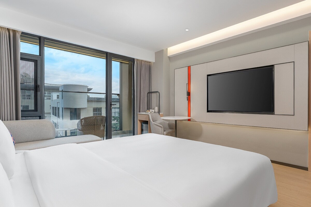 Een moderne hotelkamer met een groot bed, een bureau, een stoel en een aan de muur bevestigde televisie.