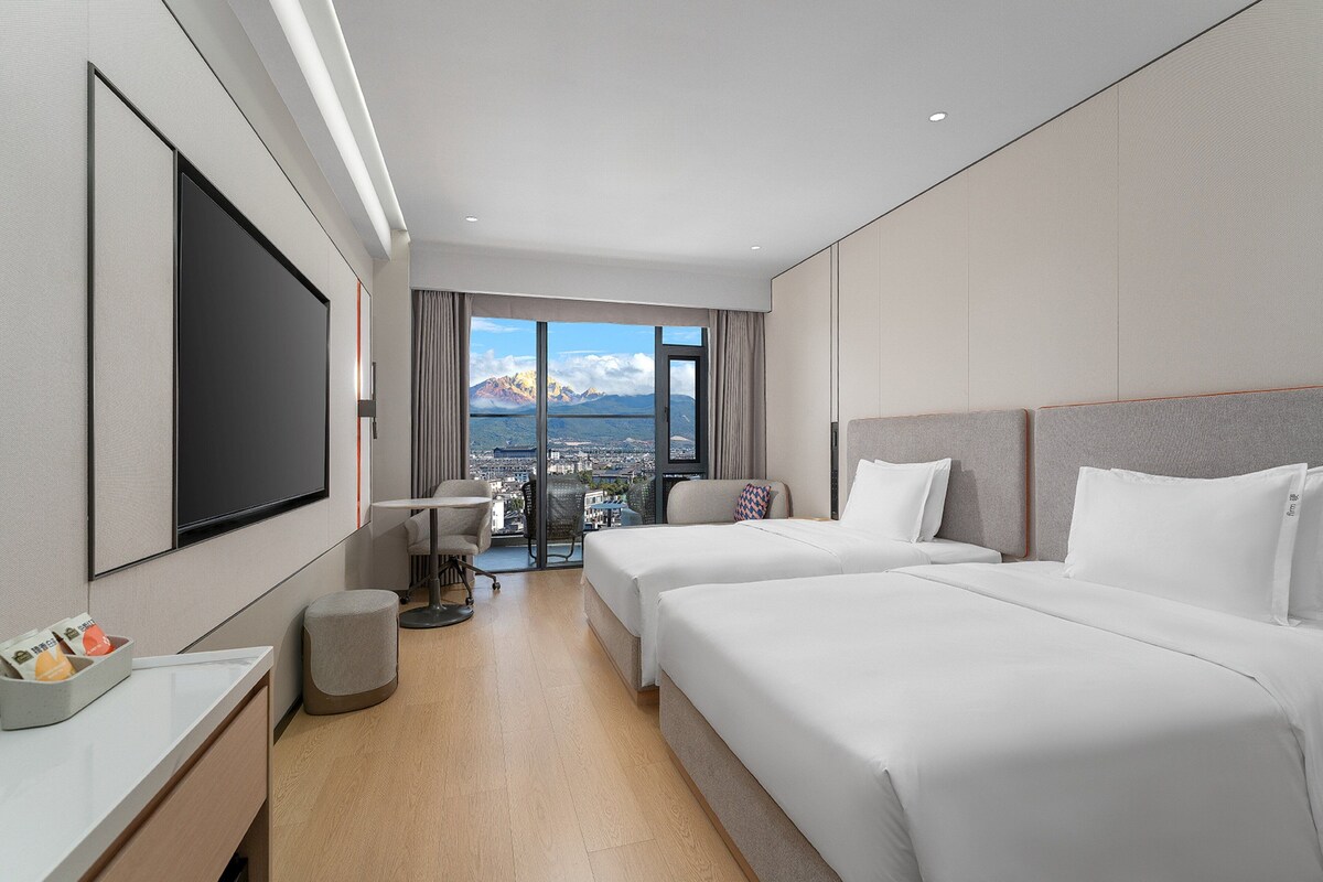 Een hotelkamer met twee bedden, een televisie, een bureau en uitzicht op bergen.