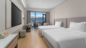 A hotel room with two beds, a TV, a desk, and a view of mountains.