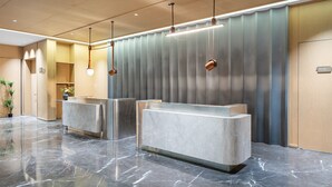 Un área de recepción con suelo de mármol, dos mostradores y una pared de paneles verticales.
