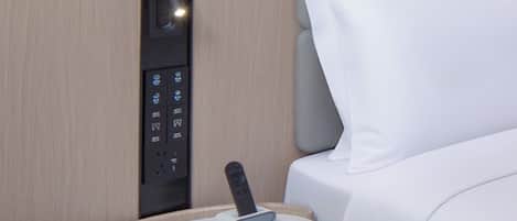 Habitación de hotel con panel de control para los servicios, una mesita de noche con control remoto y una cama bien hecha.