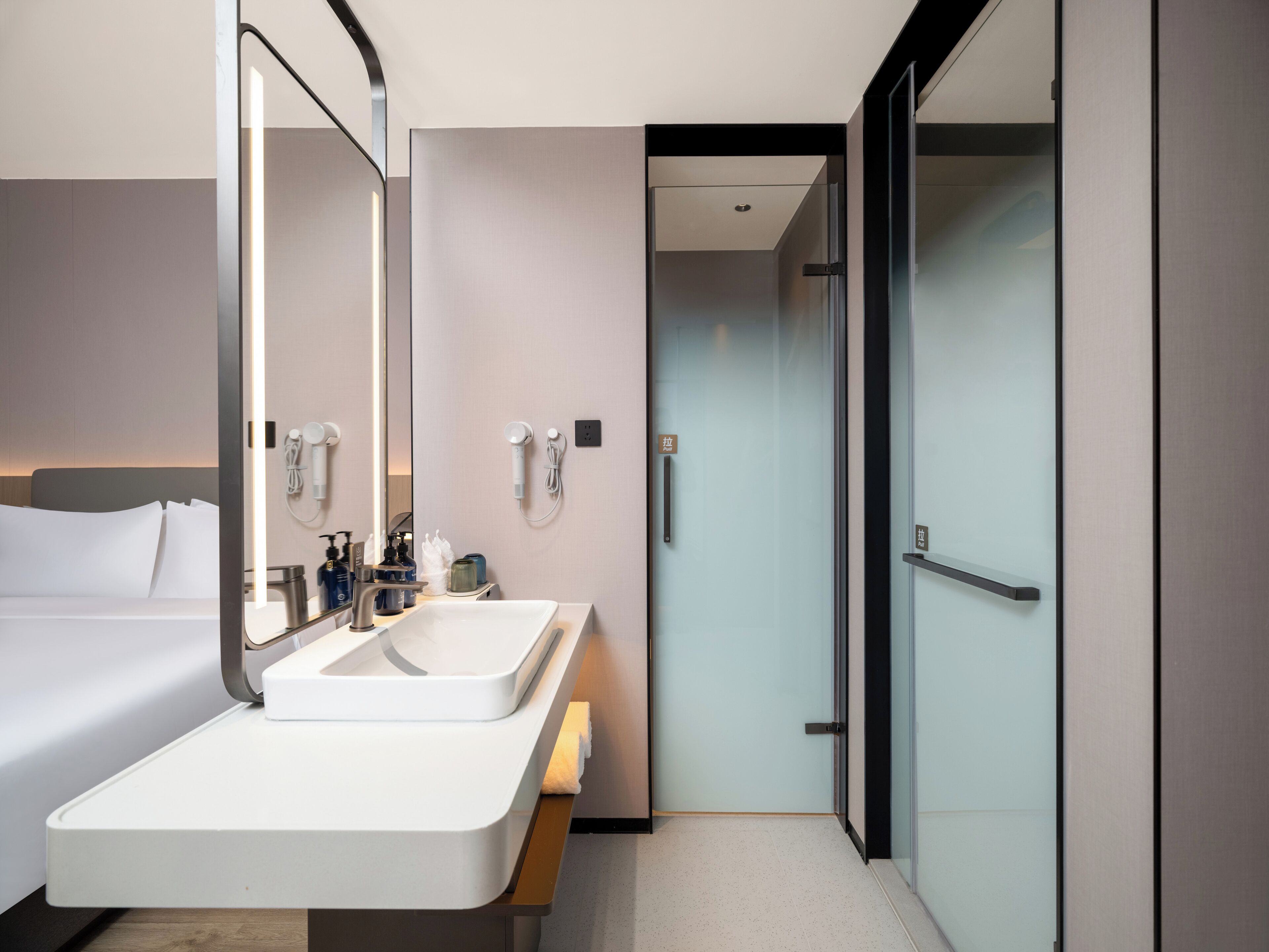 A modern hotel bathroom with a large mirror, two sinks, and a shower area.