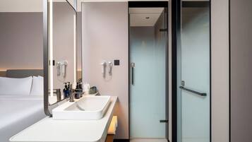 A modern hotel bathroom with a large mirror, two sinks, and a shower area.