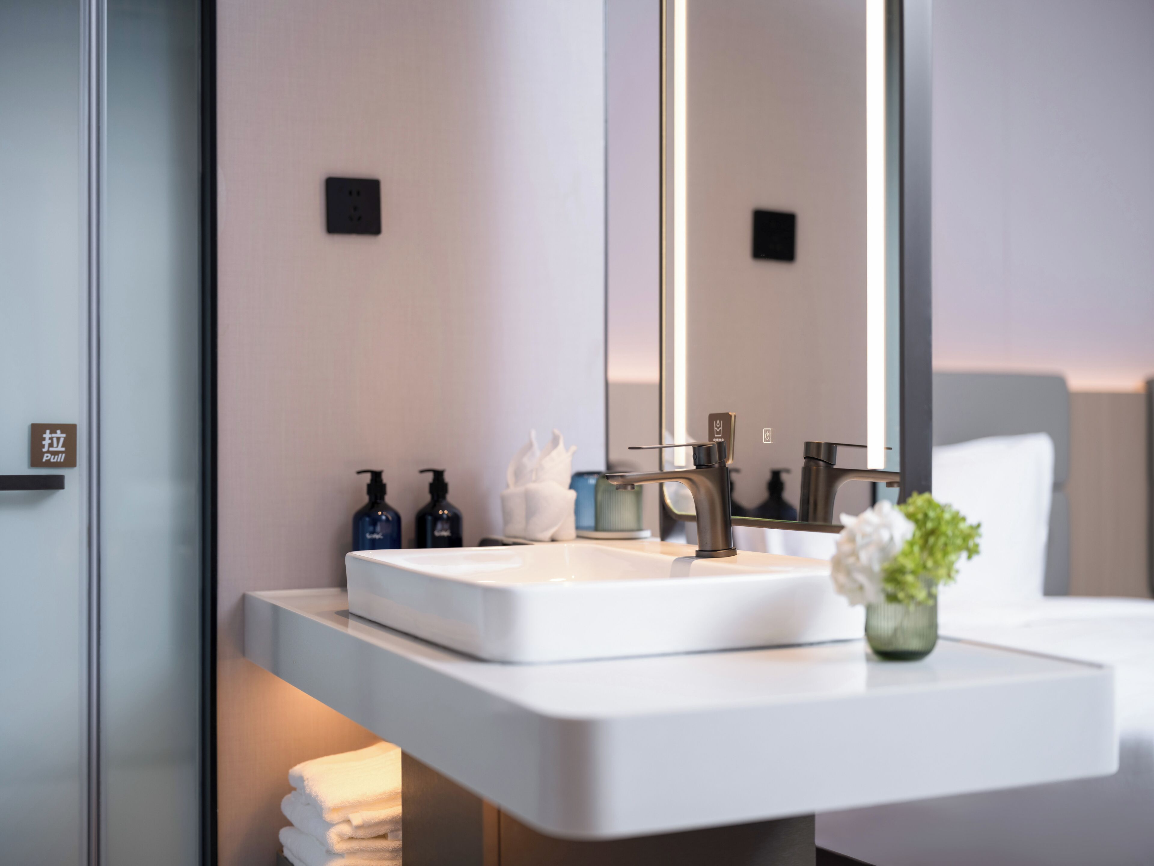 Un baño moderno con un lavabo blanco, dos dispensadores de jabón, un perchero para toallas y un espejo.