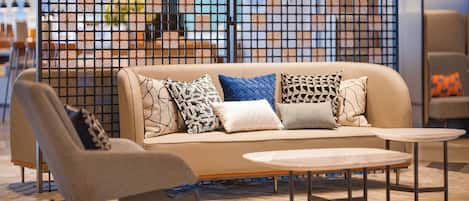 A modern living area with a beige sofa, patterned cushions, a small round table, and a chair.