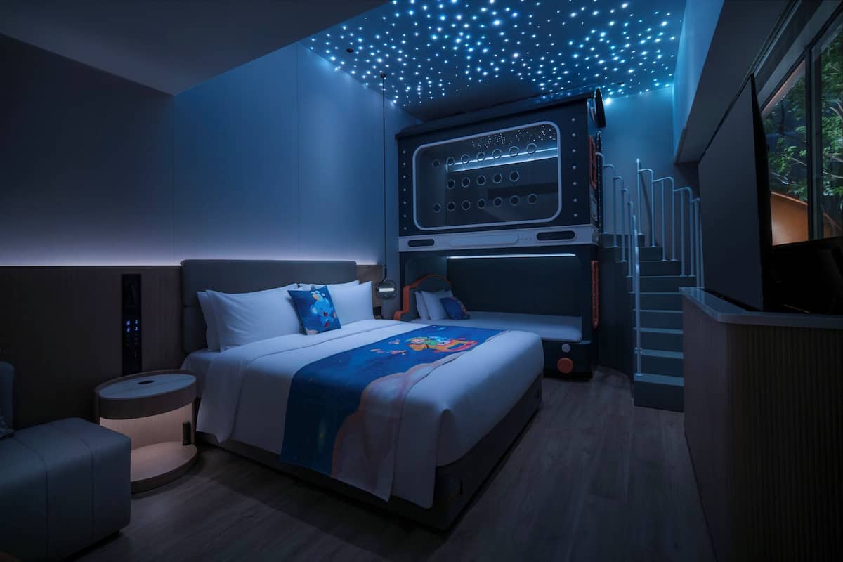 A modern hotel room with a large bed, a bedside table, a nightstand, and a ceiling with star-like lights.