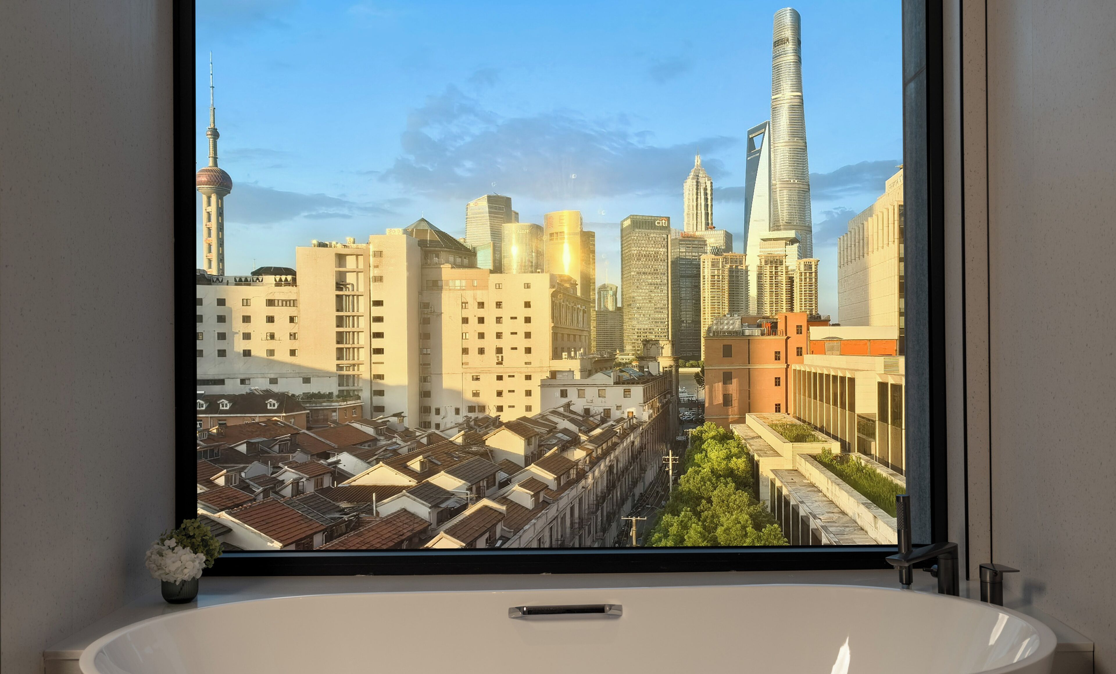 A bathroom with a large window overlooking a cityscape with high-rise buildings and a distinctive tower.