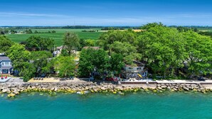 A coastal property with a wooden deck, stone walls, and a view of the sea. - Peaceful Point Lakehouse with Hot tub (Leamington)