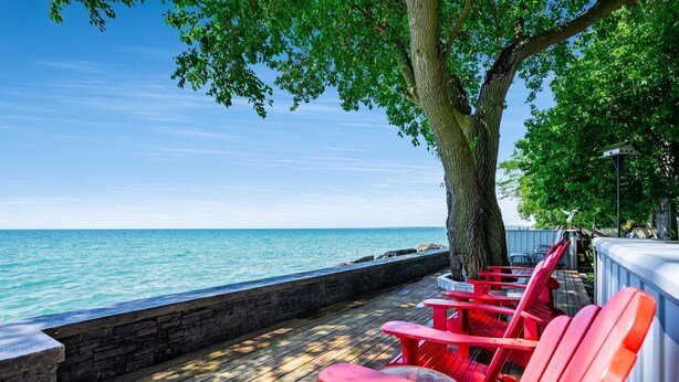 A wooden deck with red chairs and tables overlooking a body of water. - Peaceful Point Lakehouse with Hot tub (Leamington)