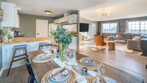 A modern kitchen with white cabinets, a wooden island, and a dining area set for six with woven placemats and a vase with blue flowers. - ColdPlunge/ HotTub/ Firepit/ BBQ/ Pet Friendly/ SunsetViews near Yosemite (Coarsegold)