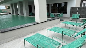 Zona de piscina con sillones y mesas, una piscina y un área de estar cubierta.