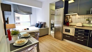 Una cocina compacta con electrodomésticos modernos, un área de comedor con una mesa lista para dos personas y un sofá en el salón contiguo.