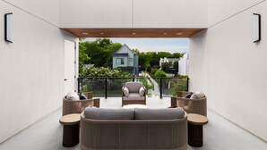 A modern outdoor seating area with a sofa, armchairs, and round tables, overlooking a residential street. - Casa Sol - Heated Pool, Outdoor Living & Design (Austin)