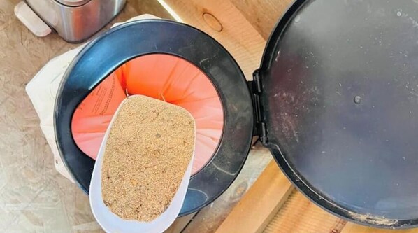 A portable cooking device with a black lid and a white tray containing a brown substance, possibly food, placed on a wooden surface.