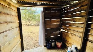 Une cabane en bois avec une porte donnant sur l’extérieur. À l’intérieur, on trouve deux seaux et une paire de chaussures.
