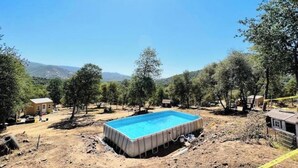 Une piscine rectangulaire entourée d’arbres, avec un sol rocailleux et aride.