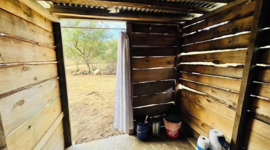 Una cabaña de madera con una puerta que da al exterior. En el interior, hay dos cubetas y un par de zapatos.