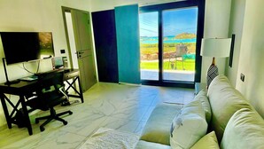 Un soggiorno moderno con un divano, una scrivania e una televisione. Una grande finestra offre vista su un paesaggio.