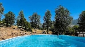 A clear blue pool surrounded by trees and a white poolside area.
