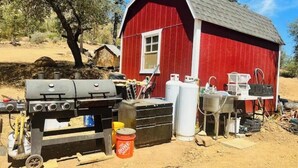 A red wooden structure with a chimney, a barbecue grill, and various containers and tools.