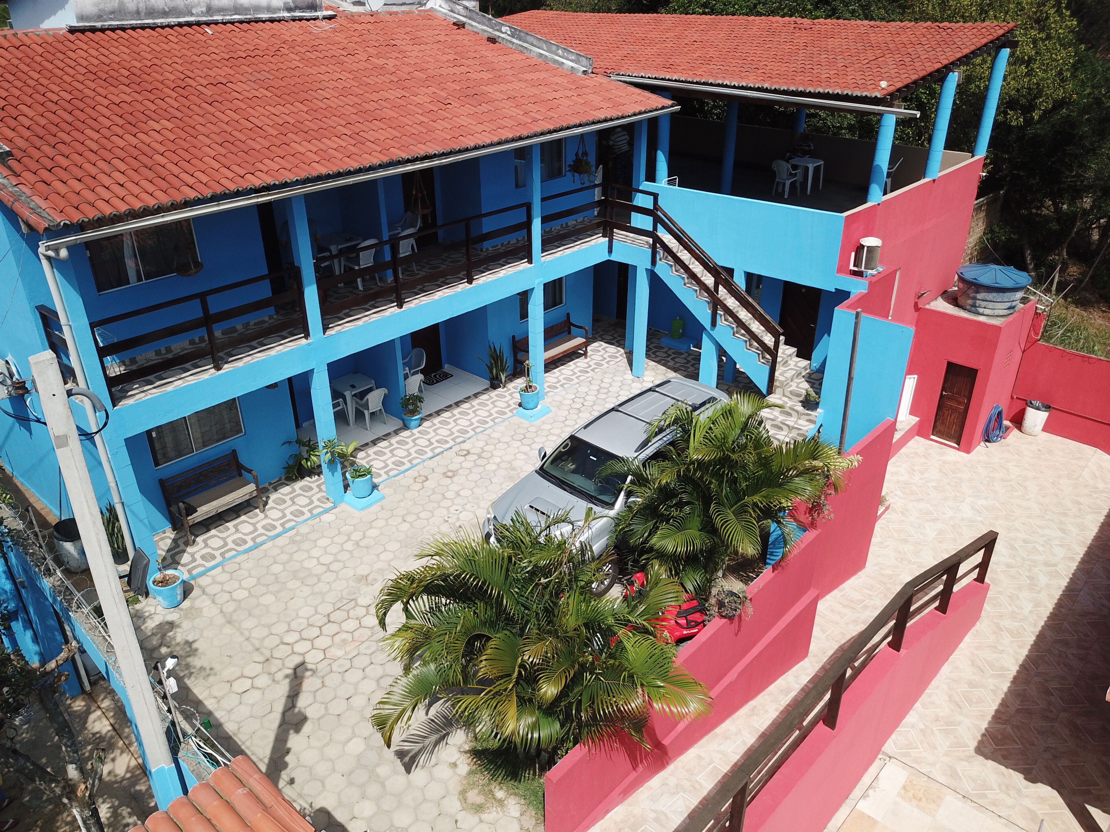 Un edificio a più piani con esterni blu e rossi, una zona relax all'aperto coperta e un'auto parcheggiata.