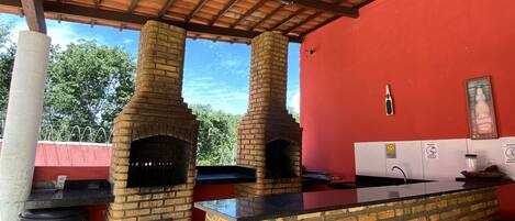 An outdoor kitchen area with two brick ovens, a countertop, and a red wall.