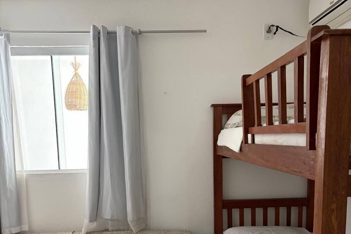 Ein Zimmer mit einem Etagenbett, einem Einzelbett mit gemustertem Bettbezug und einem Fenster mit Vorhängen.