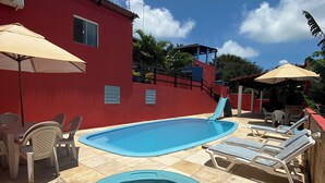 A red building with a swimming pool and a hot tub. There are lounge chairs and umbrellas around the pool. - Pousada Estrela do Norte (Tibau do Sul)