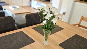 A dining table with a vase of white flowers and black placemats.
