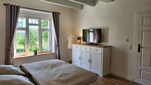 A bedroom with a bed, a TV on a cabinet, a window with curtains, and a door.