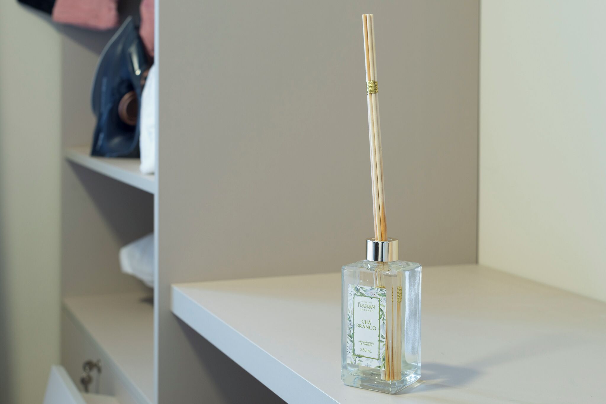 Eine klare Glasflasche mit einem Holzschilf auf einem weißen Regal.