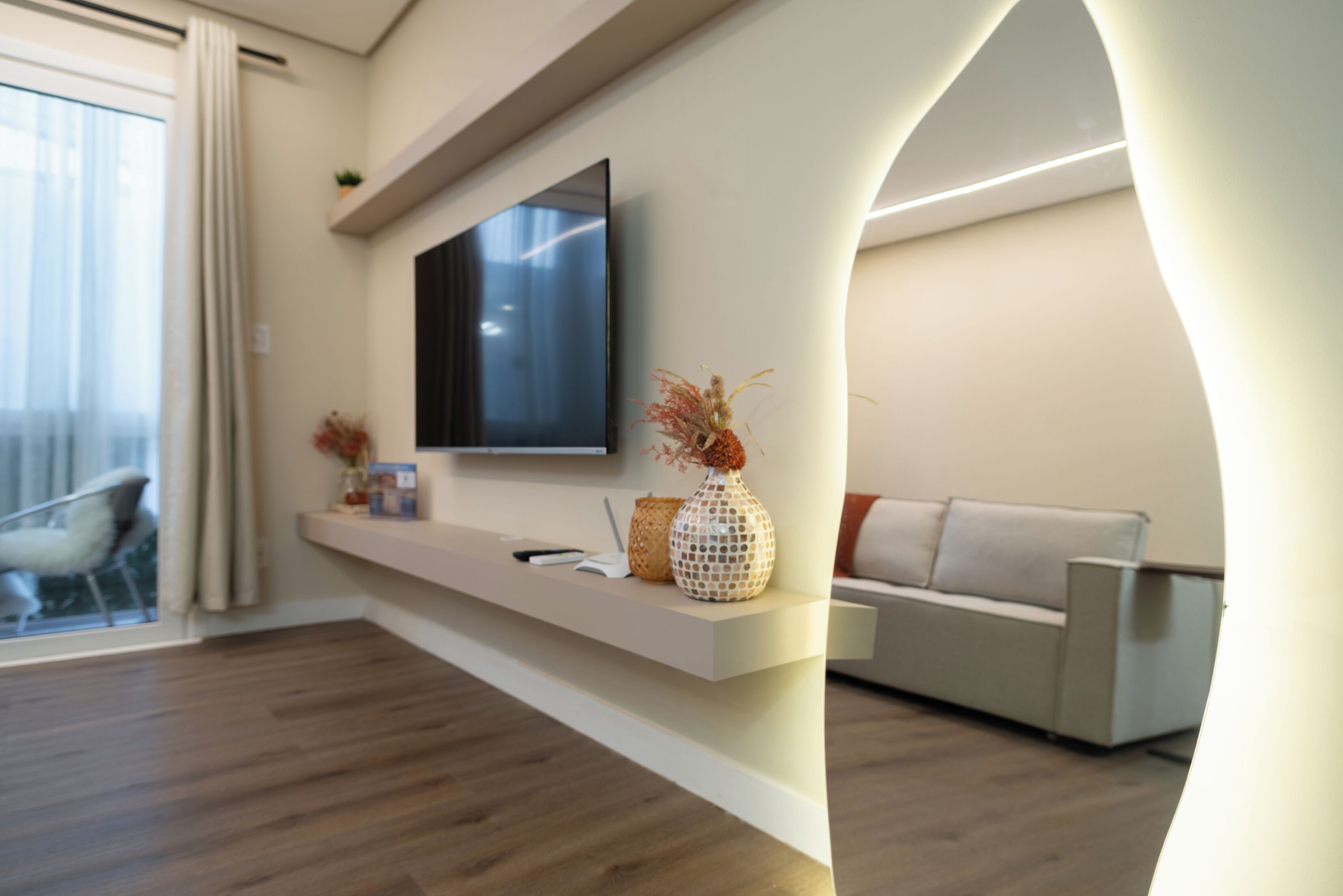 A modern living room with a flat-screen TV mounted on the wall, a white sofa, and a wooden floor.