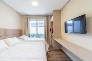Camera d'albergo con due letti, una TV a parete, un armadio e una finestra con tende.