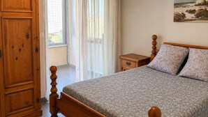 A bedroom with a wooden bed, a nightstand, a wardrobe, and a window with sheer curtains.