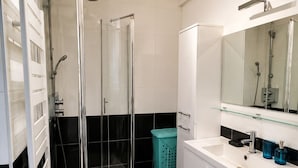 A modern bathroom with a glass-enclosed shower, a white vanity with a mirror, and a washing machine.
