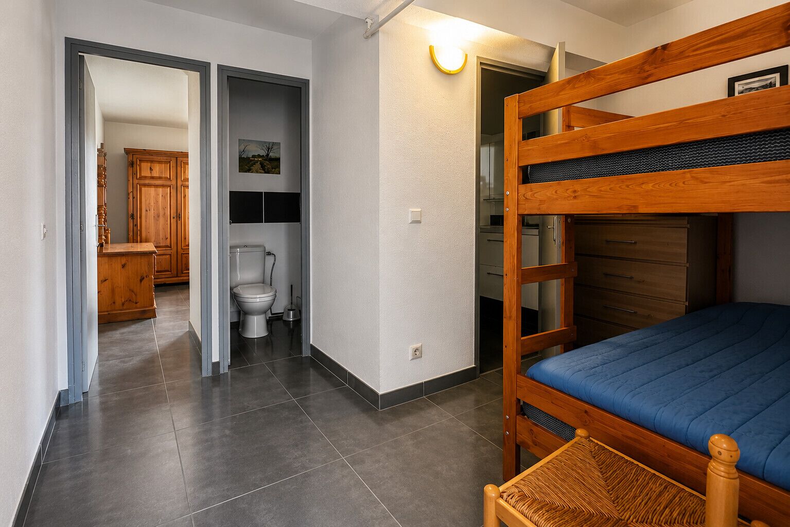 Een kamer met een stapelbed, een houten kast, een toilet en een kleine badkamer.