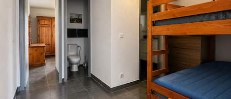 Een kamer met een stapelbed, een houten kast, een toilet en een kleine badkamer.