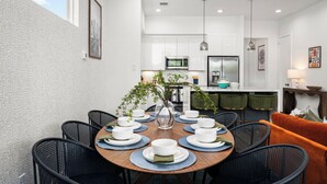 Un comedor moderno con una mesa redonda preparada para seis personas, rodeada de sillas negras. Un jarrón con follaje verde está colocado en el centro.