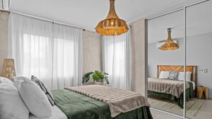 A modern bedroom with a large bed, a mirror, a hanging light fixture, and a potted plant. - 2 Boho Apartments in 1 Listing: With Pool and Steps to Beach (San Juan)