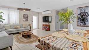 A modern living room with a grey sofa, a wooden coffee table, a patterned rug, and a large painting on the wall. - 2 Boho Apartments in 1 Listing: With Pool and Steps to Beach (San Juan)